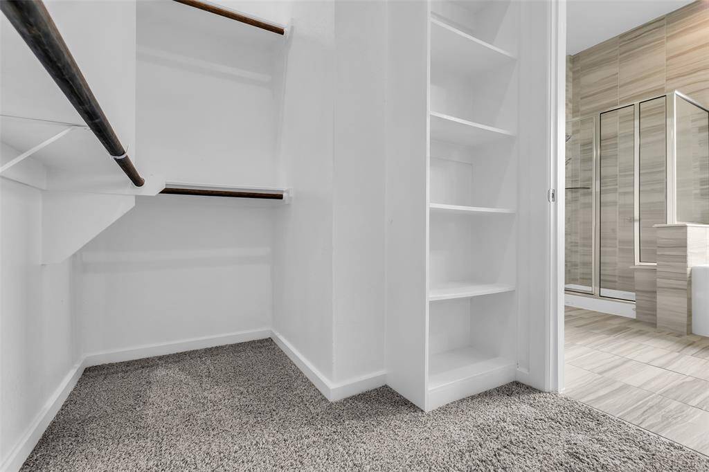 Adjacent to the bathroom, the walk-in closet features built-in shelves and a carpeted floor for added storage and convenience.