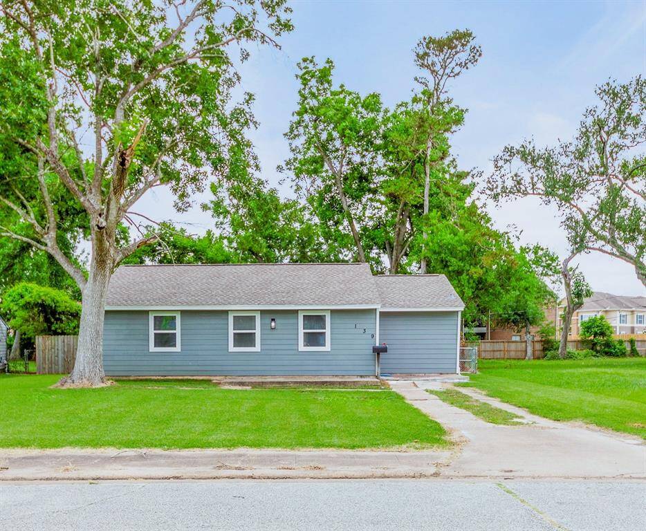 Mature trees provide shade, and a paved driveway leads to the entrance. The property offers a peaceful suburban setting