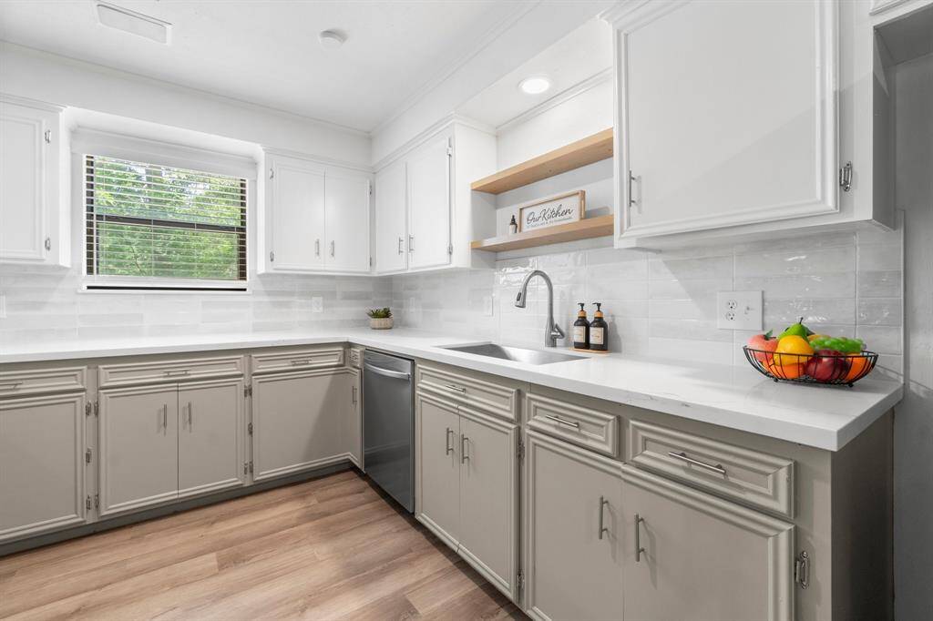 This kitchen has a large window overlooking the yard and boasts a newt tiled backsplash. Floating shelves above the sink add extra design appeal.