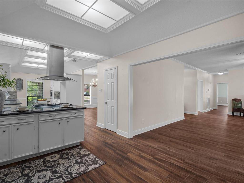 This photo showcases a spacious, open-concept interior with a modern kitchen featuring a sleek island and stainless steel hood. The room has porcelain wood floors, ample natural light, and neutral walls, offering a versatile and inviting living space.