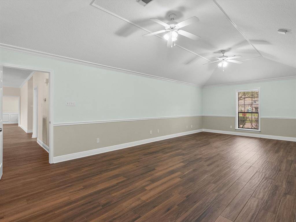 Spacious Primary bedroom with high ceilings ,porcelain wood flooring, and neutral walls. Features two ceiling fans and a large window for natural light.