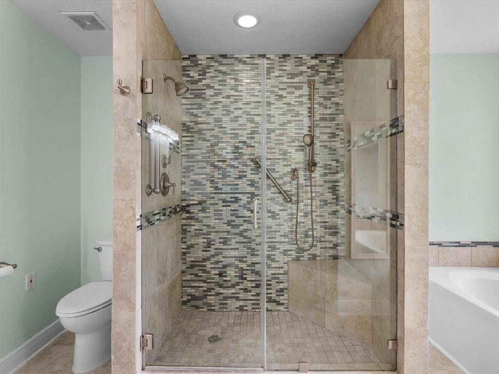 This shower is enhanced with elegant mosaic tile and glass doors, complemented by a neutral walls and adjacent bathtub.