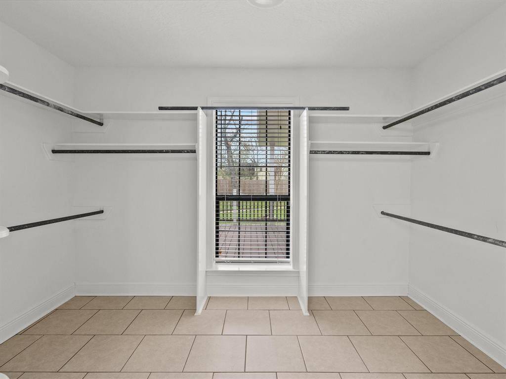 Primary bedroom walk-in closet offers more than enough shelving and hanging space, featuring a window with blinds for natural light and tiled flooring.