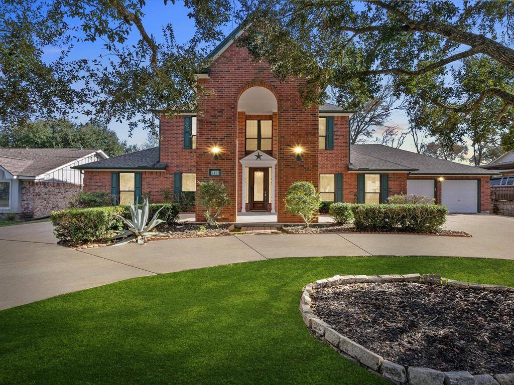 This charming two-story brick home features a welcoming front porch, well-maintained landscaping, and dual circular driveways leading to a two-car garage. The exterior is complemented by lush greenery and mature trees, offering a serene and inviting curb appeal.