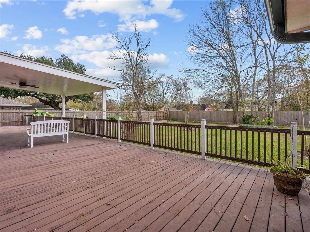 This photo showcases a spacious backyard with a large wooden deck and a covered patio area. The yard is enclosed by a wooden fence, offering privacy and a serene view of trees and open sky—ideal for outdoor relaxation and entertaining.