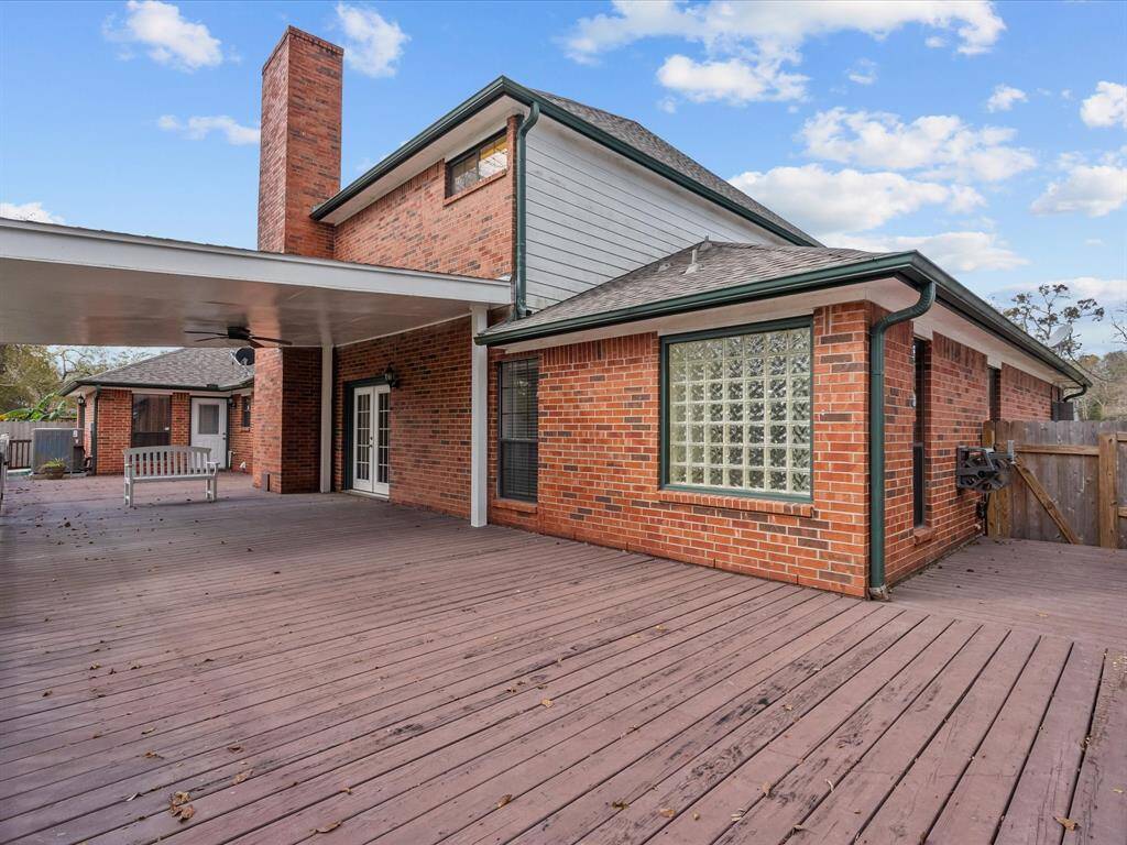 This photo showcases a spacious brick home with a large wooden deck, perfect for outdoor gatherings. It features a covered area and a glass block window for added style and natural light.
