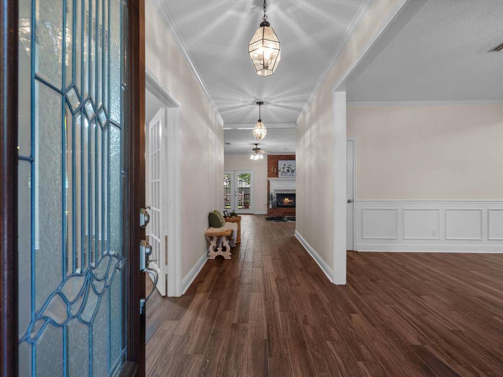 a welcoming entryway with elegant porcelain wood like flooring, leading to a bright living area featuring a brick fireplace. The space is accentuated by stylish light fixtures and decorative wainscoting, offering a blend of warmth and sophistication.