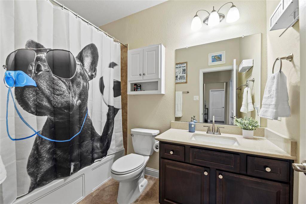 Elongated commode, brushed nickel lighting and plumbing fixtures and tile flooring and surround.