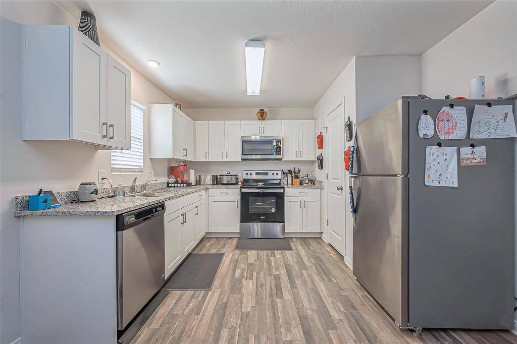 This kitchen features modern appliances, white cabinetry, and granite countertops. It has a spacious layout with ample storage and a sleek, light wood floor. Ideal for cooking and entertaining.