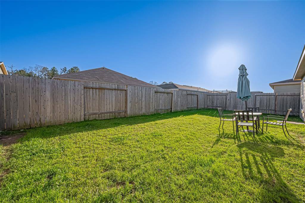 Spacious backyard with lush green grass, enclosed by a wooden fence. Features a patio set with an umbrella, perfect for outdoor relaxation and entertaining.