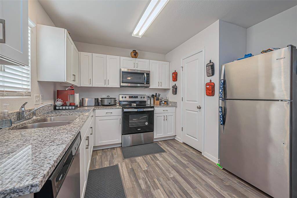 This kitchen features modern stainless steel appliances, white cabinetry, and granite countertops. It has a clean, bright look with ample storage and counter space, complemented by wood-style flooring.