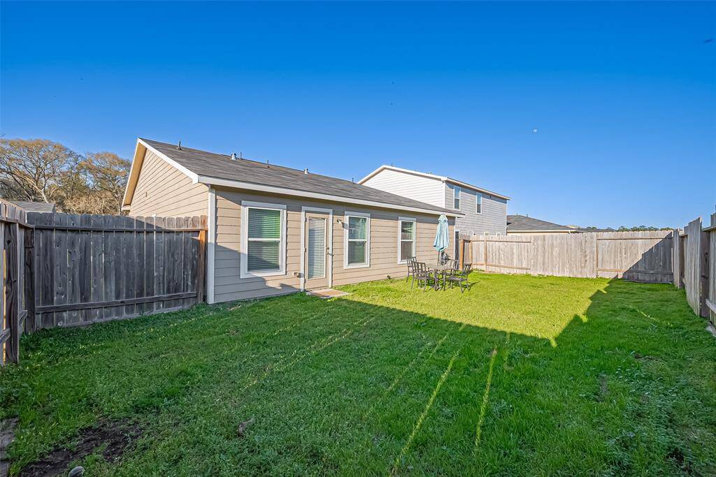 This photo shows a cozy backyard with a well-maintained lawn, surrounded by a wooden fence. The house features a modest patio area with outdoor seating, perfect for relaxation or entertaining.