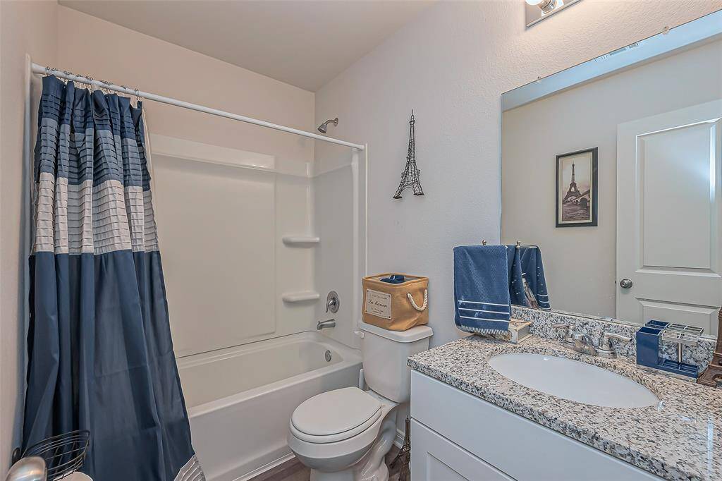 This bathroom features a modern design with a granite countertop, a large mirror, and a combination shower-tub. It has a stylish blue and white color scheme with Paris-themed decor, creating a clean and inviting space.