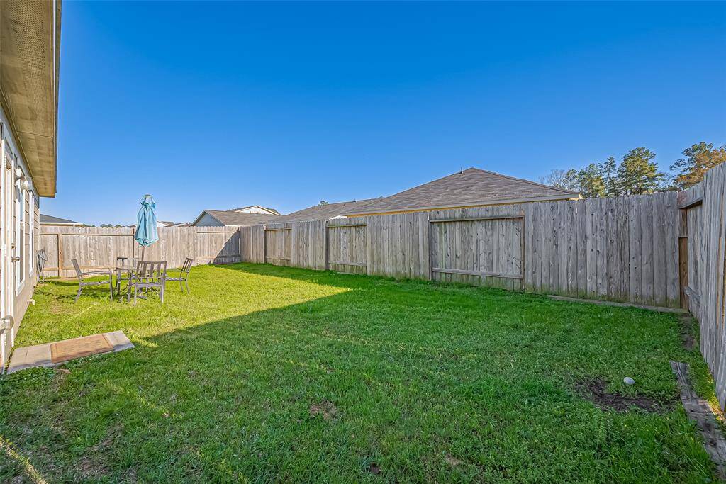 Spacious backyard with a well-maintained lawn, surrounded by a wooden fence for privacy. Includes a patio area with outdoor seating and an umbrella, ideal for relaxation and entertaining.