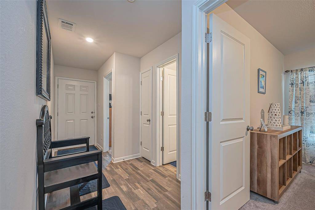 This photo features a welcoming entryway with laminate wood flooring, leading to adjacent rooms. The area is well-lit with neutral walls, a decorative bench, and a storage unit. The decor includes a framed mirror and wall art, creating a cozy first impression.