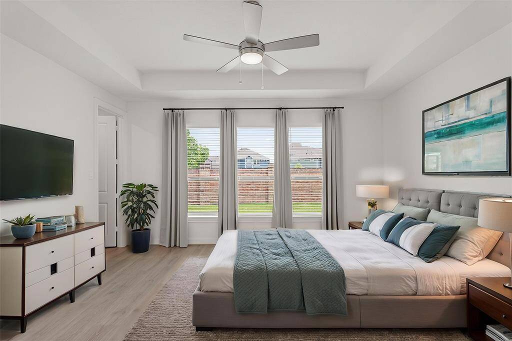 Virtually Staged: Unwind in this cozy primary bedroom with LVP floors, a tray ceiling with a ceiling fan, and large windows with privacy blinds.