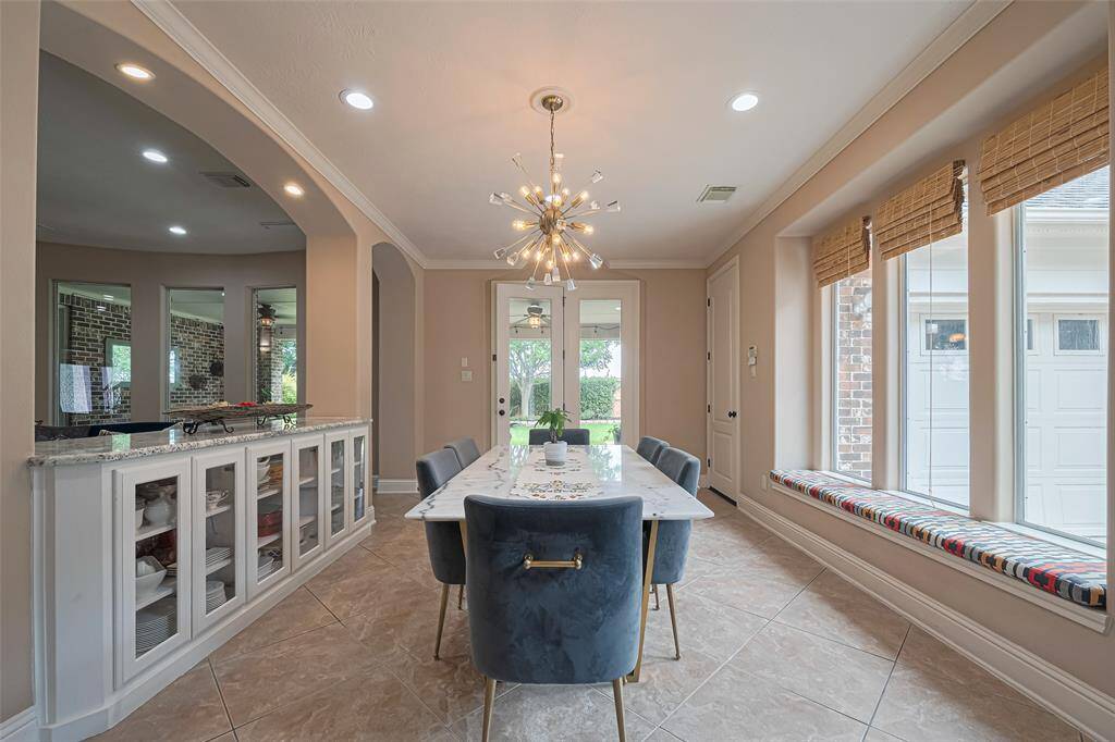 Located just off the kitchen, it features a striking modern chandelier, neutral tile flooring, and open archways that flow effortlessly into the living and kitchen areas