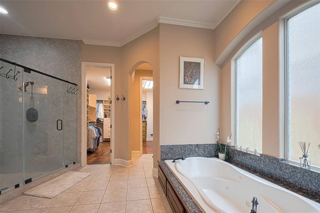 Spa-inspired primary bath offers a deep soaking tub beneath frosted arched windows, dual vanities, granite countertops, and a private dressing area