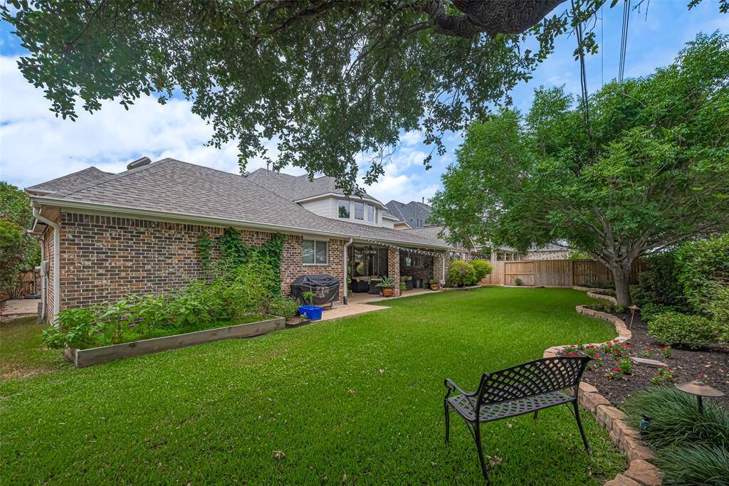 tep into a private backyard retreat with lush green grass, mature trees providing natural shade, and professionally landscaped flower beds lined with stone borders