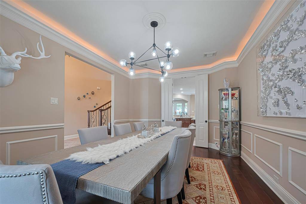 The formal dining room features intricate wall molding, rich crown molding with ambient cove lighting, and a contemporary chandelier that makes a bold statement