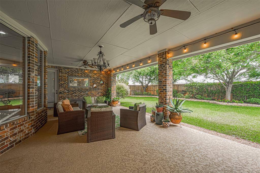 Outfitted with dual ceiling fans, a wrought iron chandelier, and café string lights, it offers ambiance and comfort in any season. Surrounded by beautifully manicured greenery, this space is a true gem for alfresco living