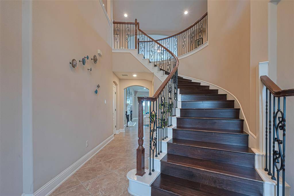 Dramatic curved staircase with wrought-iron balusters and dark wood steps creates a grand foyer entrance, complemented by high ceilings and a spacious hallway for an elegant first impression
