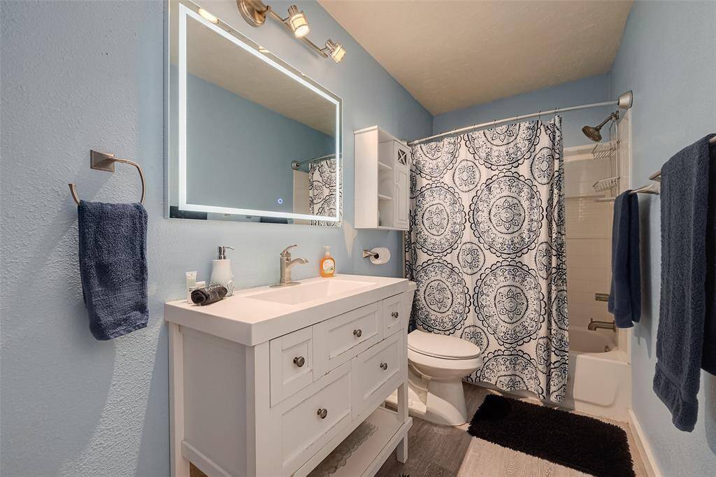 The fresh, coastal-inspired palette of soft blue and white enhances the vanity area in the bathroom, complete with a large mirror and stylish task lighting.