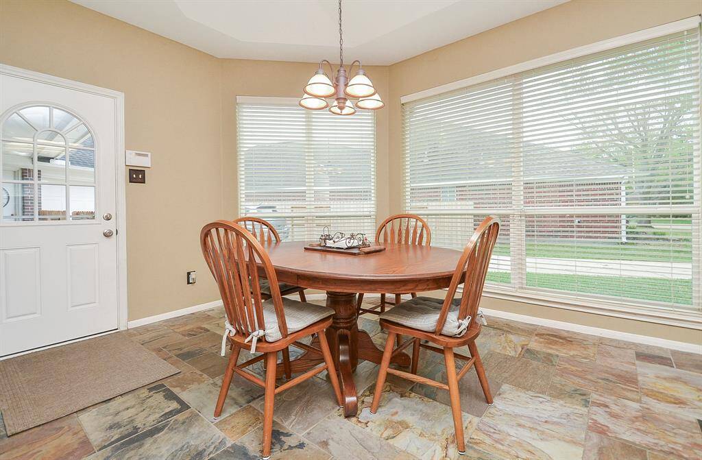 This inviting dining/breakfast area features large windows and slate floors. The space is adjacent to a door leading outside, offering easy access to the backyard.