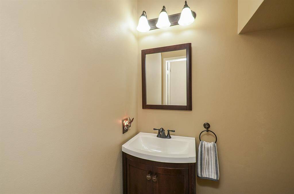 Cozy powder room featuring a sleek pedestal sink with a dark wood vanity, a simple wall-mounted mirror, and modern light fixtures above. The space is accented with neutral-toned walls.