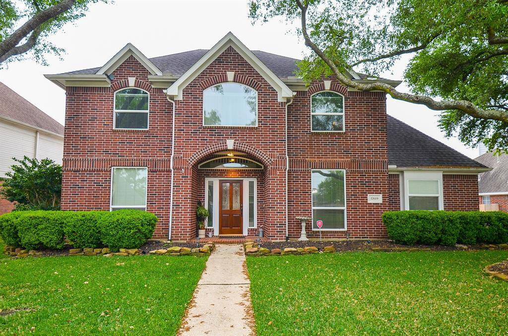 This is a charming two-story brick home with a symmetrical front facade. It features large windows, a welcoming entrance and is surrounded by well-maintained landscaping and mature trees.