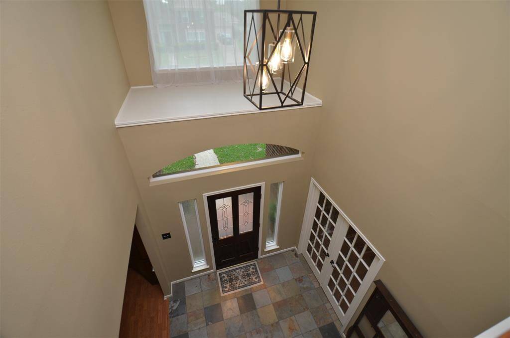 This photo showcases a spacious entryway with high ceilings, a stylish light fixture, and natural light streaming through large windows.
