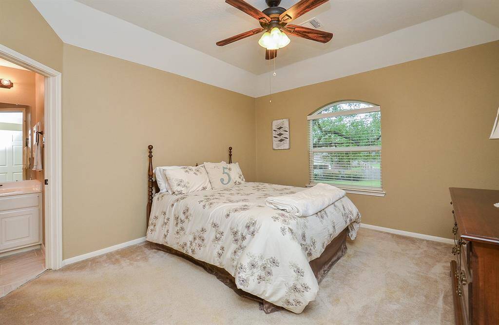 Another cozy bedroom with neutral tones, featuring a ceiling fan, carpeted floor, and a large window for natural light. Includes an en-suite bathroom for convenience.