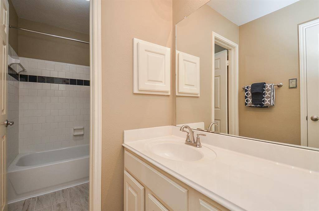 This bathroom features a bathtub with a tiled shower area, a large mirror, and a double sink vanity with modern fixtures. Neutral walls and decorative tiles add a touch of elegance.