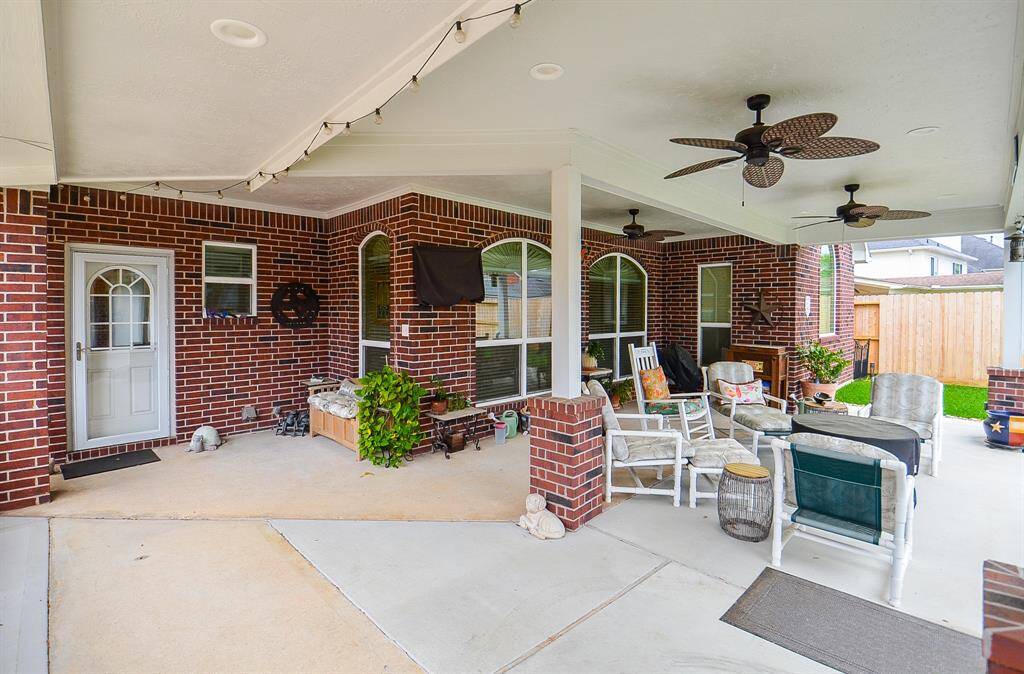 This photo showcases a spacious, covered patio with brick walls and ceiling fans, offering a cozy outdoor seating area perfect for relaxation and entertaining.