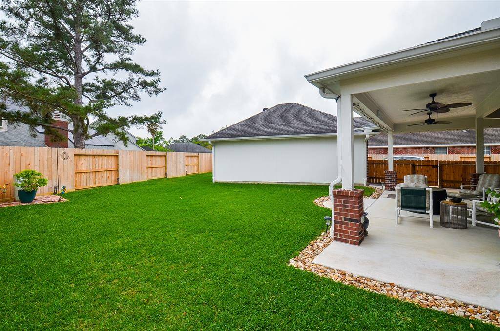 Spacious backyard with lush green lawn and a covered patio. Features a cozy seating area with ceiling fans, bordered by a wooden fence for privacy. Perfect for outdoor relaxation and entertaining.