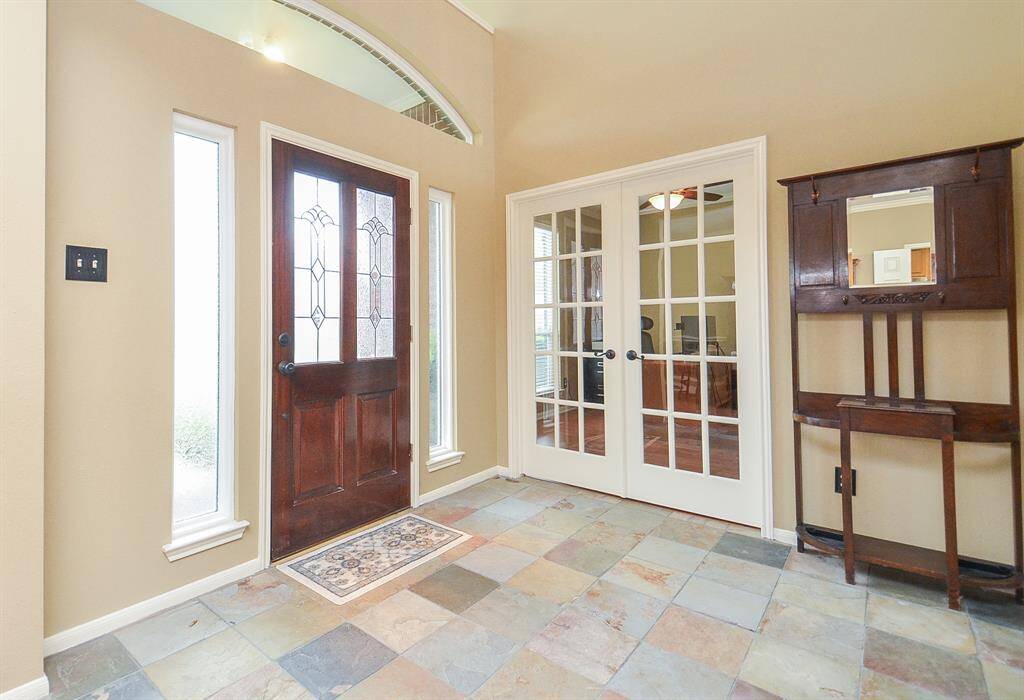 This entryway features a refinished front door with decorative glass panels, flanked by tall windows for natural light. It opens to the study with French doors.
