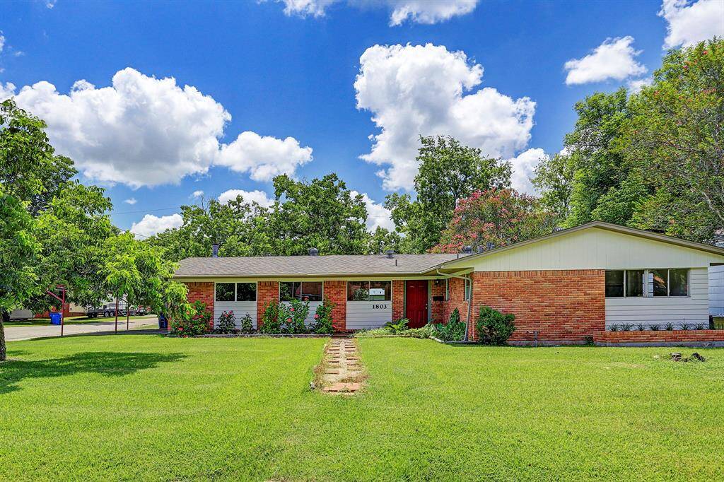 This charming single-story home features a brick exterior with a welcoming red front door. It's surrounded by a spacious, well-maintained lawn and mature trees, offering both curb appeal and shade. Perfect for families seeking a cozy and inviting suburban residence.