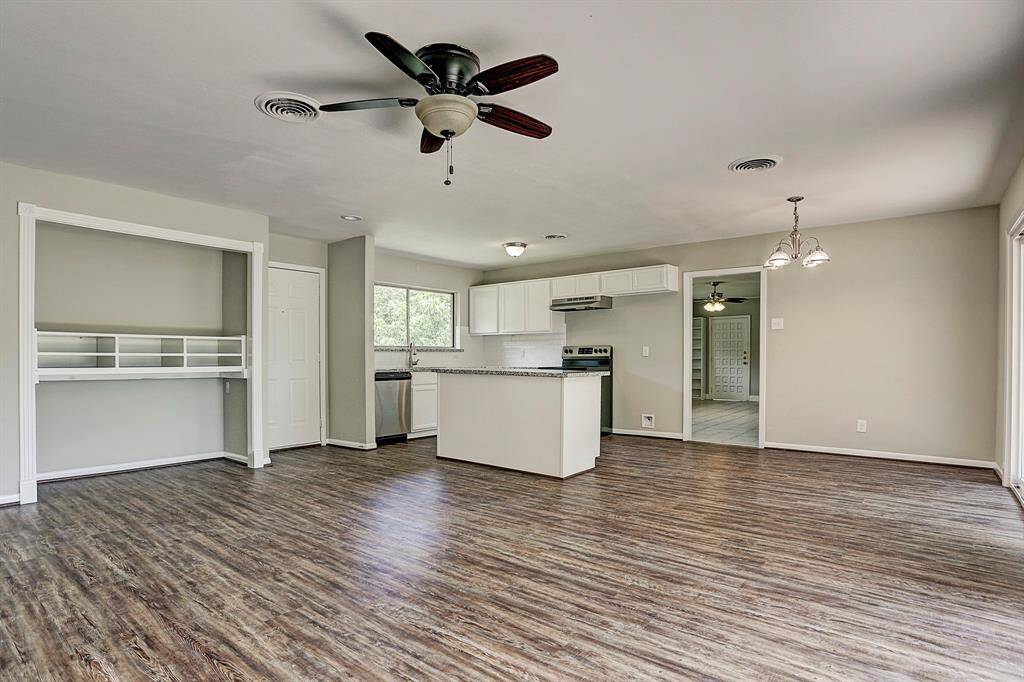 Spacious open-concept kitchen and living area with laminate wood flooring, modern ceiling fans, and ample natural light. Features an island, stainless steel appliances, and a built-in shelving unit. Neutral tones create a welcoming atmosphere.