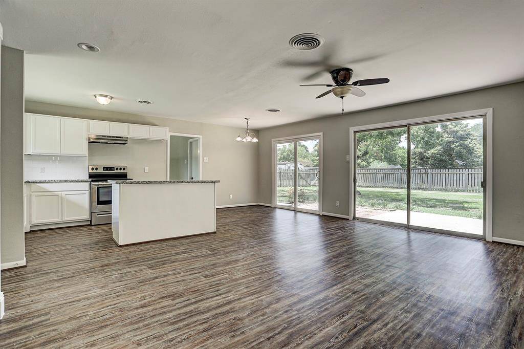 This photo showcases an open-concept kitchen and living area with modern appliances, sleek hardwood flooring, and ample natural light from large sliding glass doors that lead to a spacious backyard.