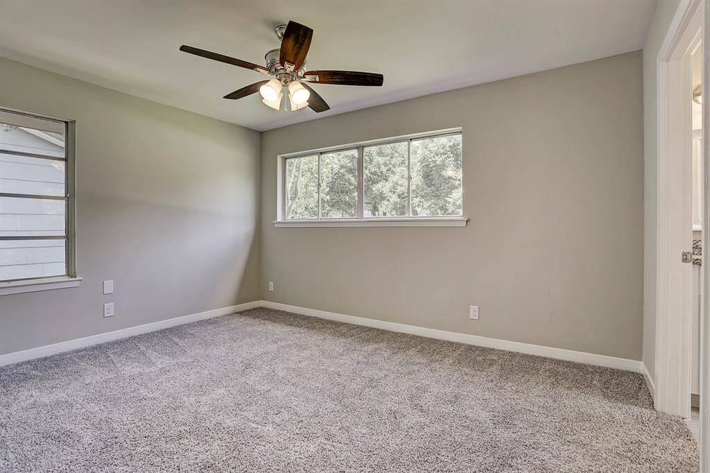 This photo showcases a bright, carpeted bedroom with neutral walls, featuring a ceiling fan and two windows that provide ample natural light.