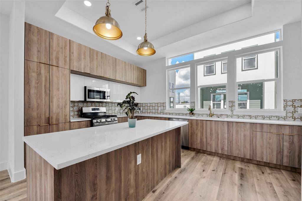 The lovely kitchen features an expanse of windows, a recessed ceiling, and brushed gold pendant lighting.