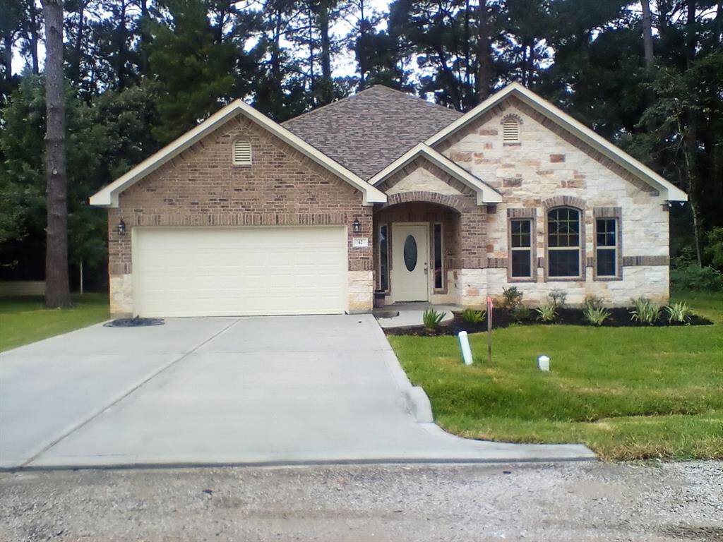 This charming single-story home features a brick and stone exterior, a two-car garage, and a welcoming front entry. It's surrounded by lush greenery, offering a serene setting.