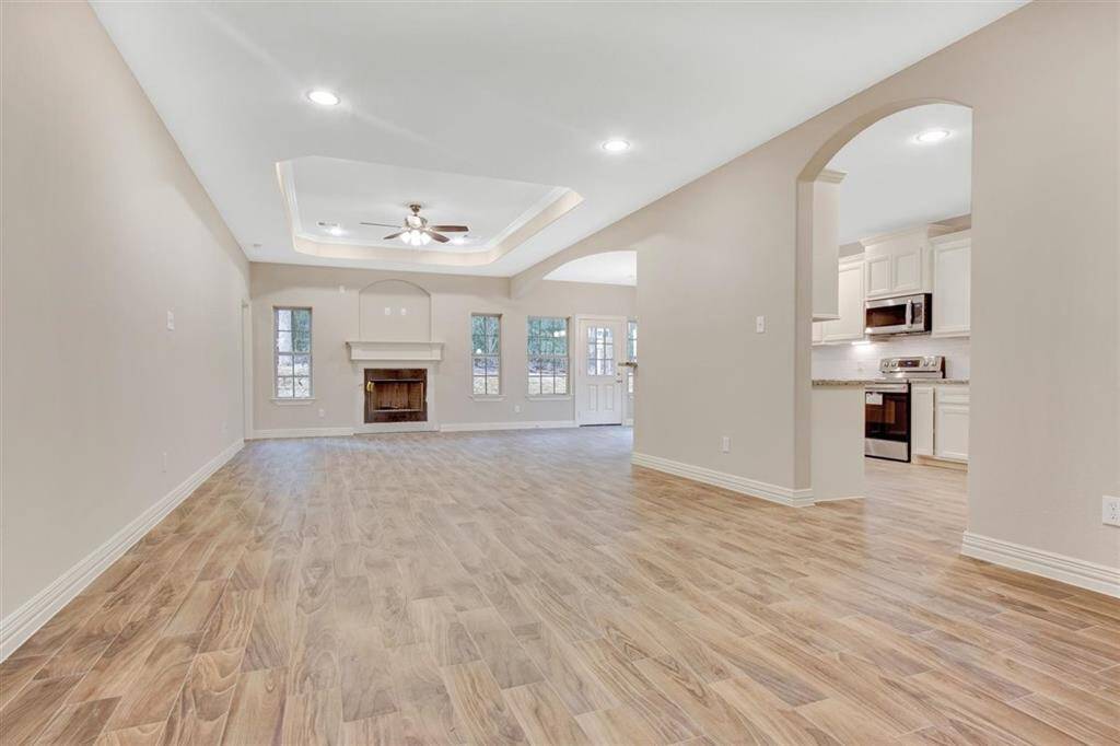 This spacious living area features wood-look flooring, a cozy fireplace, and ample natural light from multiple windows. The open layout seamlessly connects to a modern kitchen with stainless steel appliances and white cabinetry, creating an inviting space for entertaining.