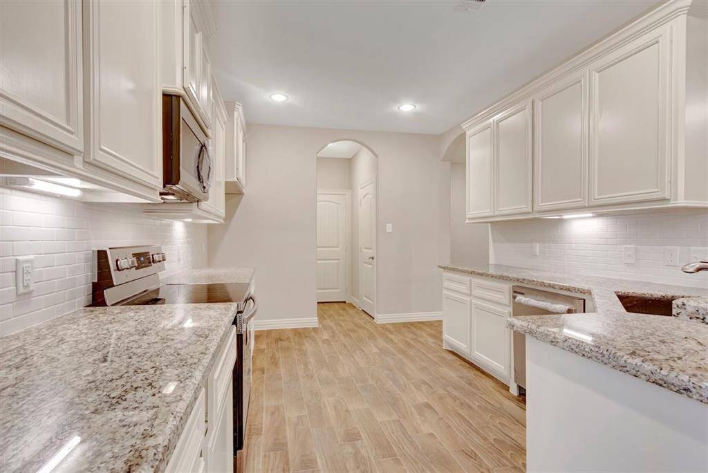 This kitchen features granite countertops, white cabinetry, and wood-style flooring. It includes modern appliances and has an open, bright layout with recessed lighting and a neutral color palette.