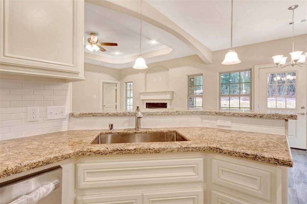 This photo showcases a bright, open-concept kitchen and living area. It features granite countertops, a large sink, stainless steel appliances, and a cozy fireplace. Natural light pours in through multiple windows, and there's a view of the outdoors. The space is inviting and ideal for entertaining.