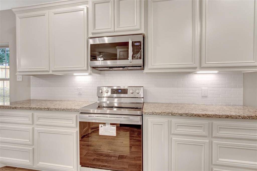 Modern kitchen featuring stainless steel appliances, white cabinetry, and a sample tile backsplash.