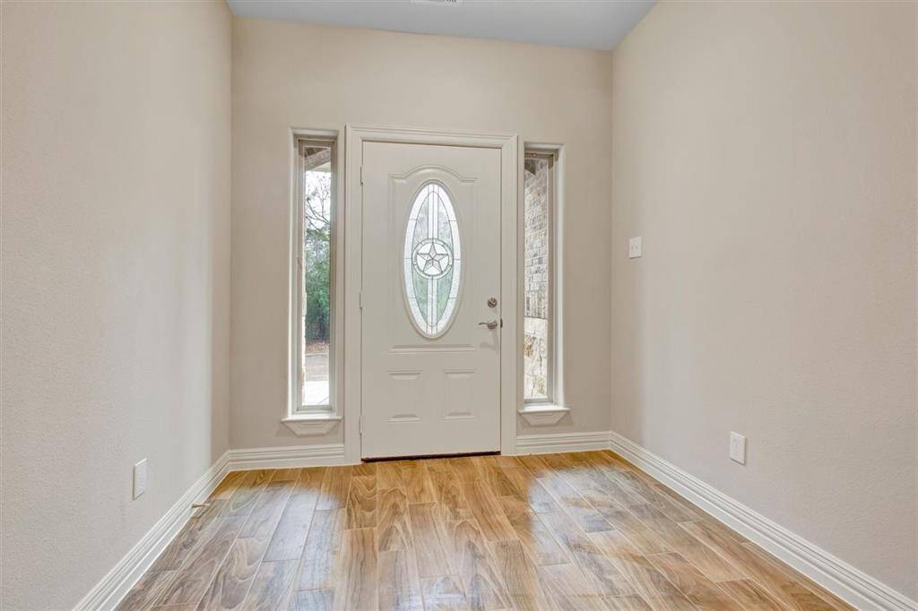 This entryway features a stylish front door with an oval glass insert and star design, flanked by narrow windows. The space is bright with natural light and has warm wood-look flooring, creating a welcoming atmosphere.