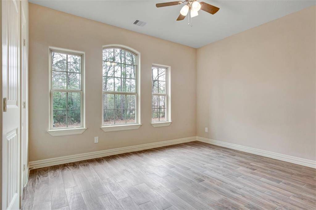 This room features three large windows that provide plenty of natural light, neutral-colored walls, wood-look tile flooring, and a ceiling fan, creating a bright and welcoming space.