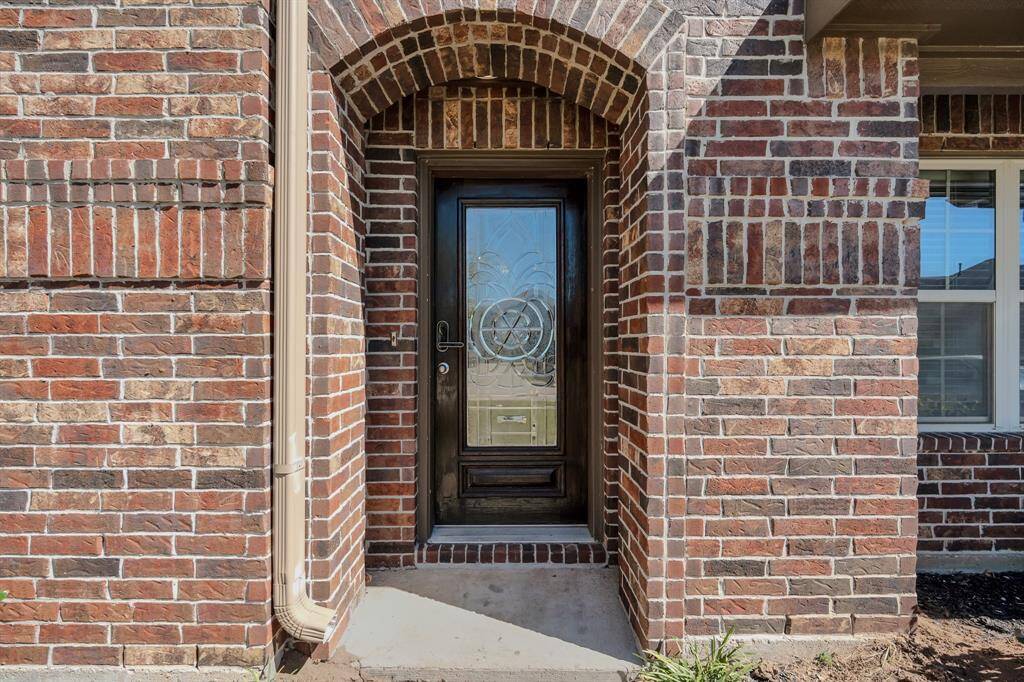 Charming brick entryway with an arched design, featuring a decorative glass front door that adds elegance and natural light to the home.
