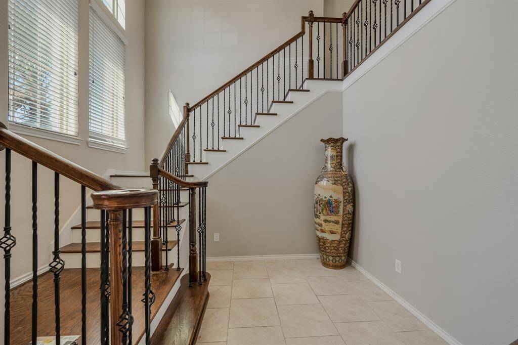 Spacious entryway with a stylish staircase featuring dark wood steps and wrought iron railings. Large windows provide natural light, and there's a decorative vase adding a touch of elegance.